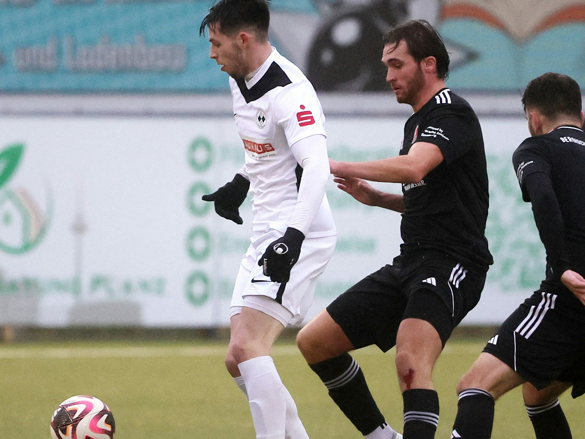 Das Bild zeigt Frechens Kai-Maxime Vranken (l.), der den Ball vor zwei Gegnern abschirmt.