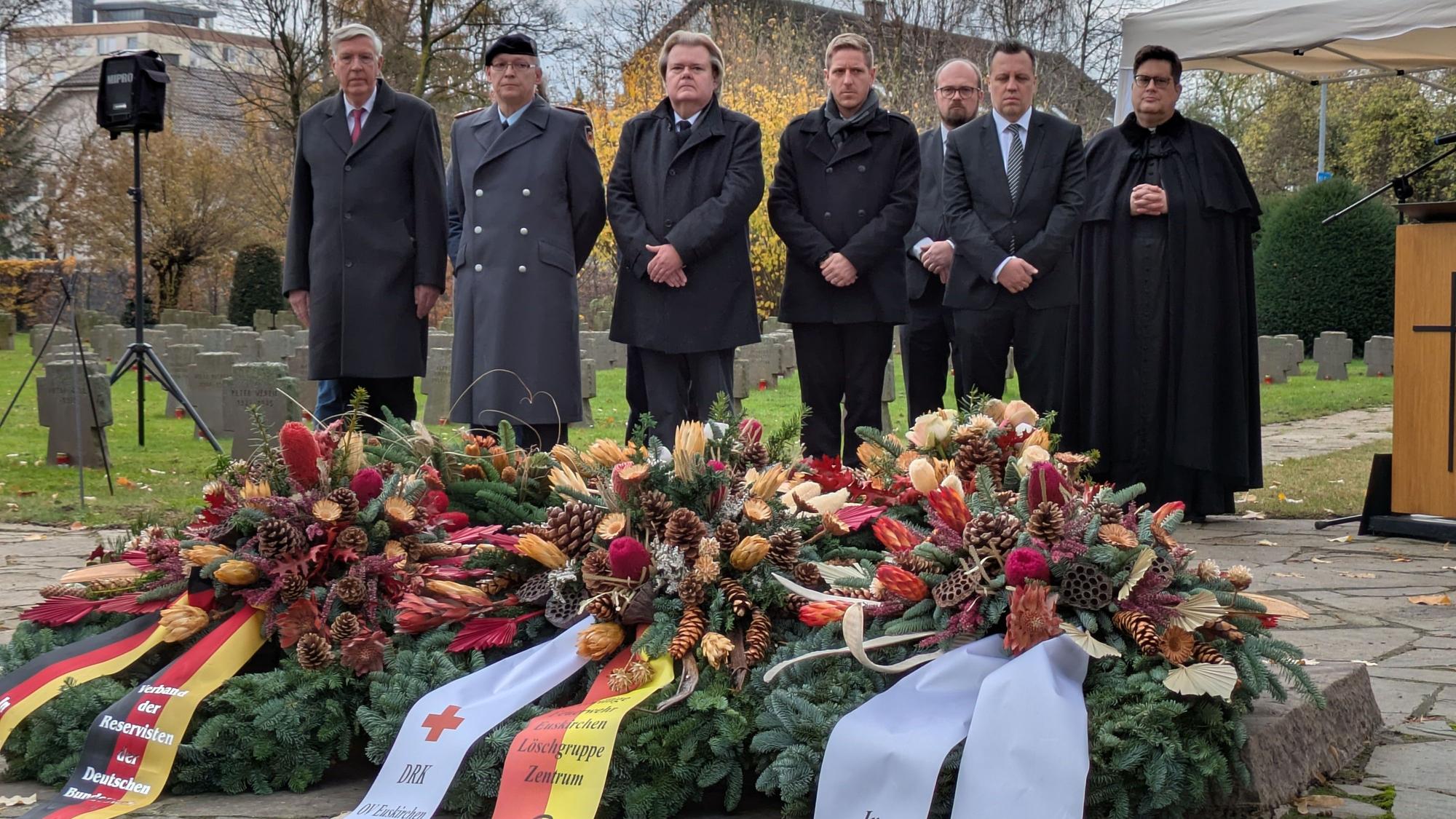 Sieben Repräsentanten stehen auf dem Friedhof, im Vordergrund die niedergelegten Kränze.