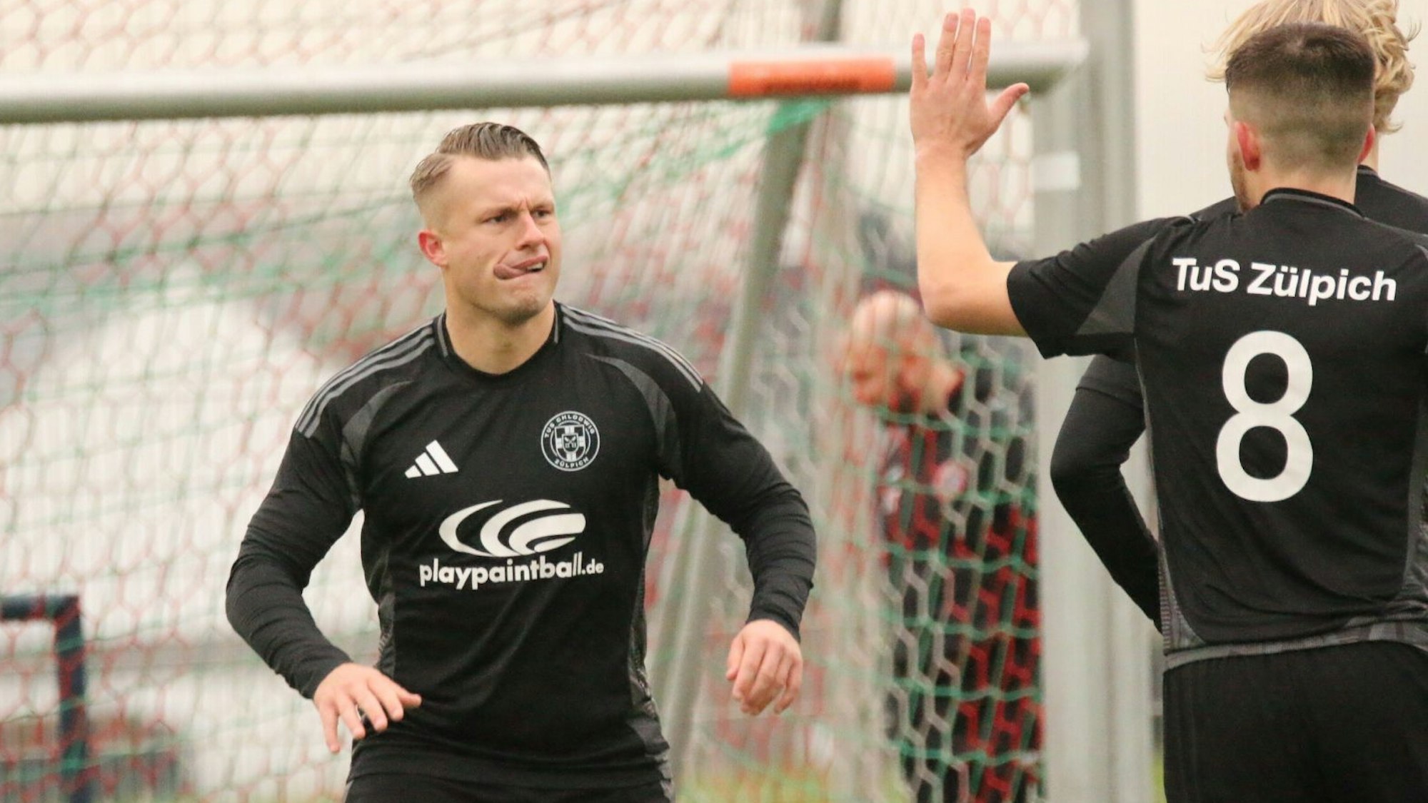 Ein Mitspieler hebt jubelnd die Hand, Marvin Iskra sieht ihn und steckt die Zunge in den Mundwinkel.