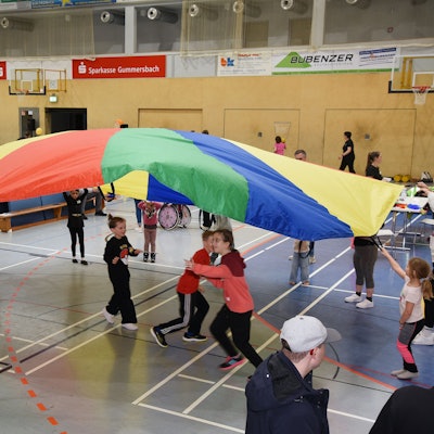 Kinder laufen unter einem Schirmtuch umher.