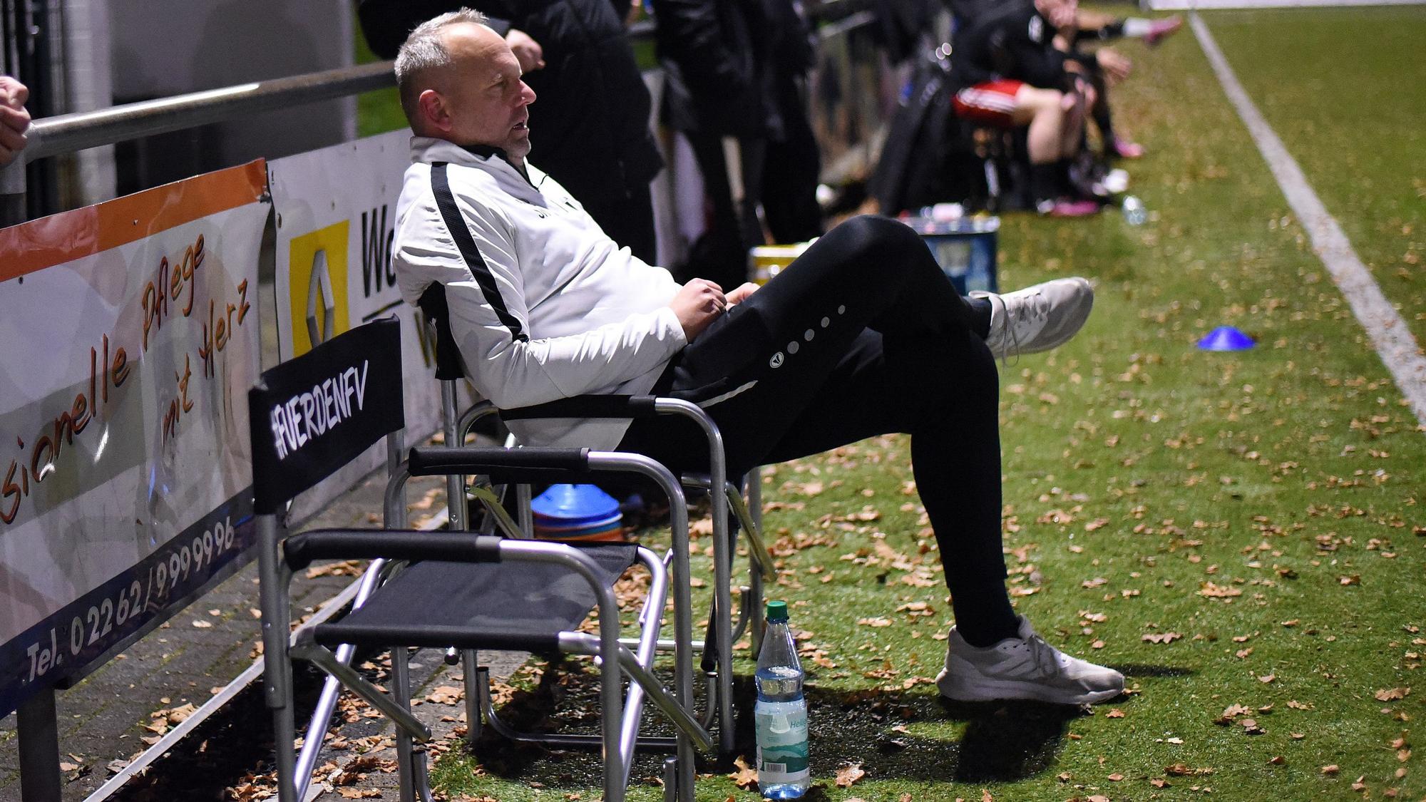 Ein Fußballtrainer sitzt während des Spiels auf einem Stuhl und beobachtet das Spiel.