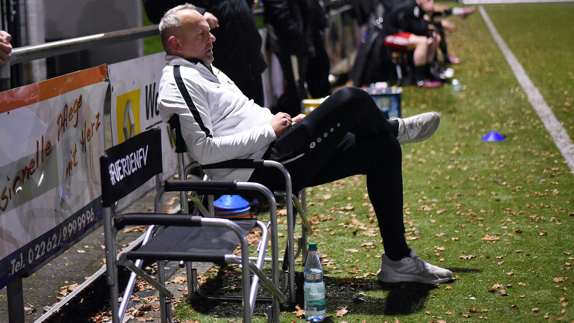 Ein Fußballtrainer sitzt während des Spiels auf einem Stuhl und beobachtet das Spiel.