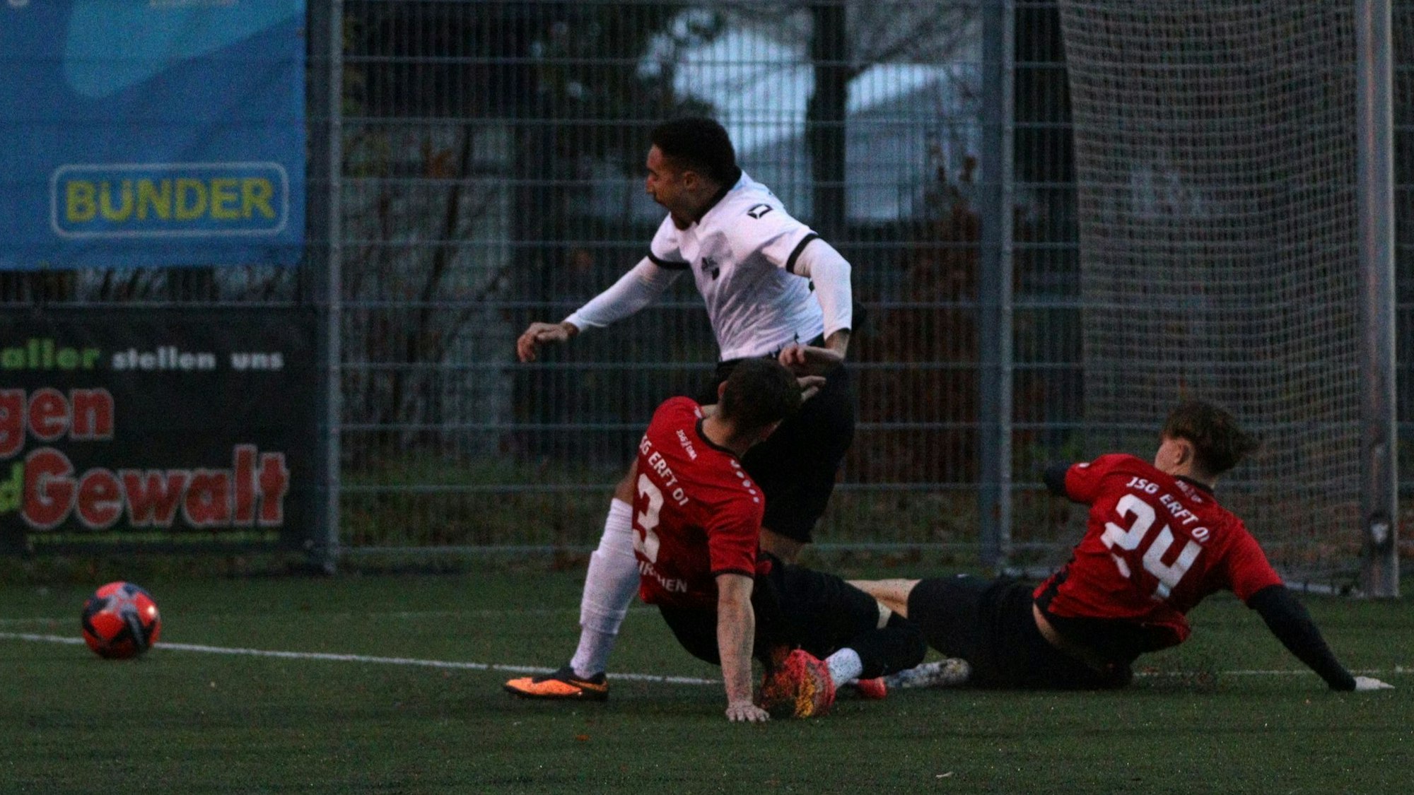Zwei Spieler der JSG Erft grätschen zum Ball und bringen dabei den gegnerischen Spieler zu Fall, der schreit.