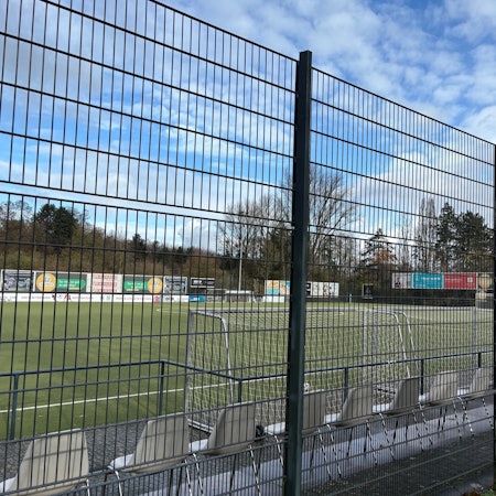 Auf dem Bild ist ein Sportplatz hinter einem Zaun zu sehen.