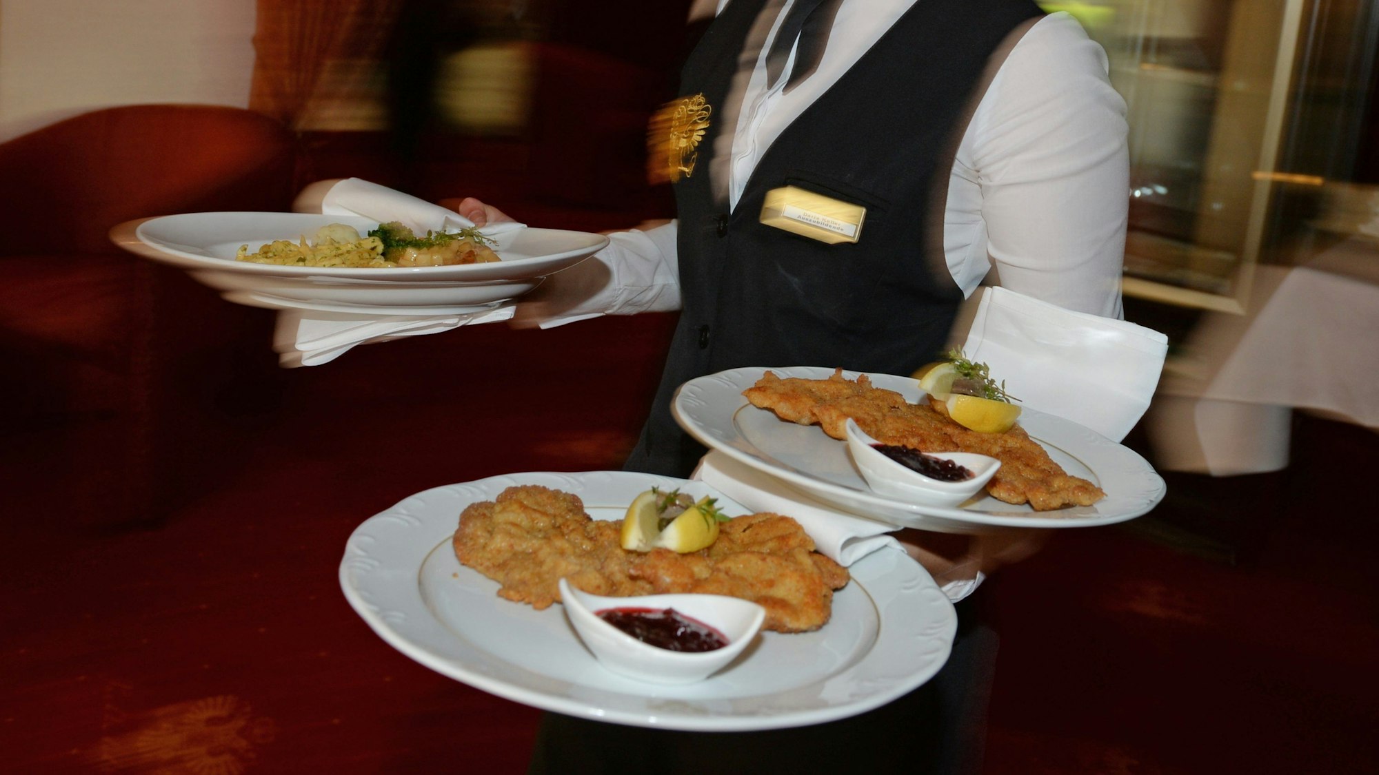 Ein Mann trägt drei Teller mit Schnitzeln.