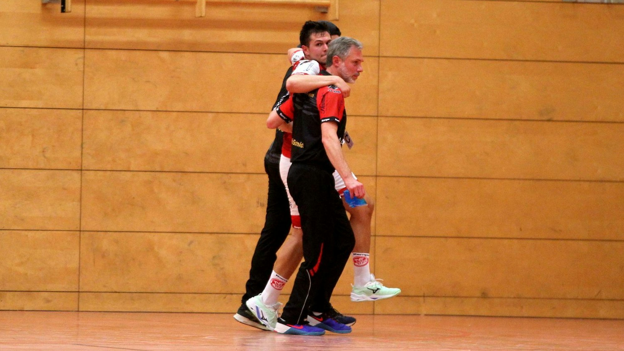 Lukas Königshoven wird von zwei Betreuern, die ihn stützen, aus der Halle begleitet.