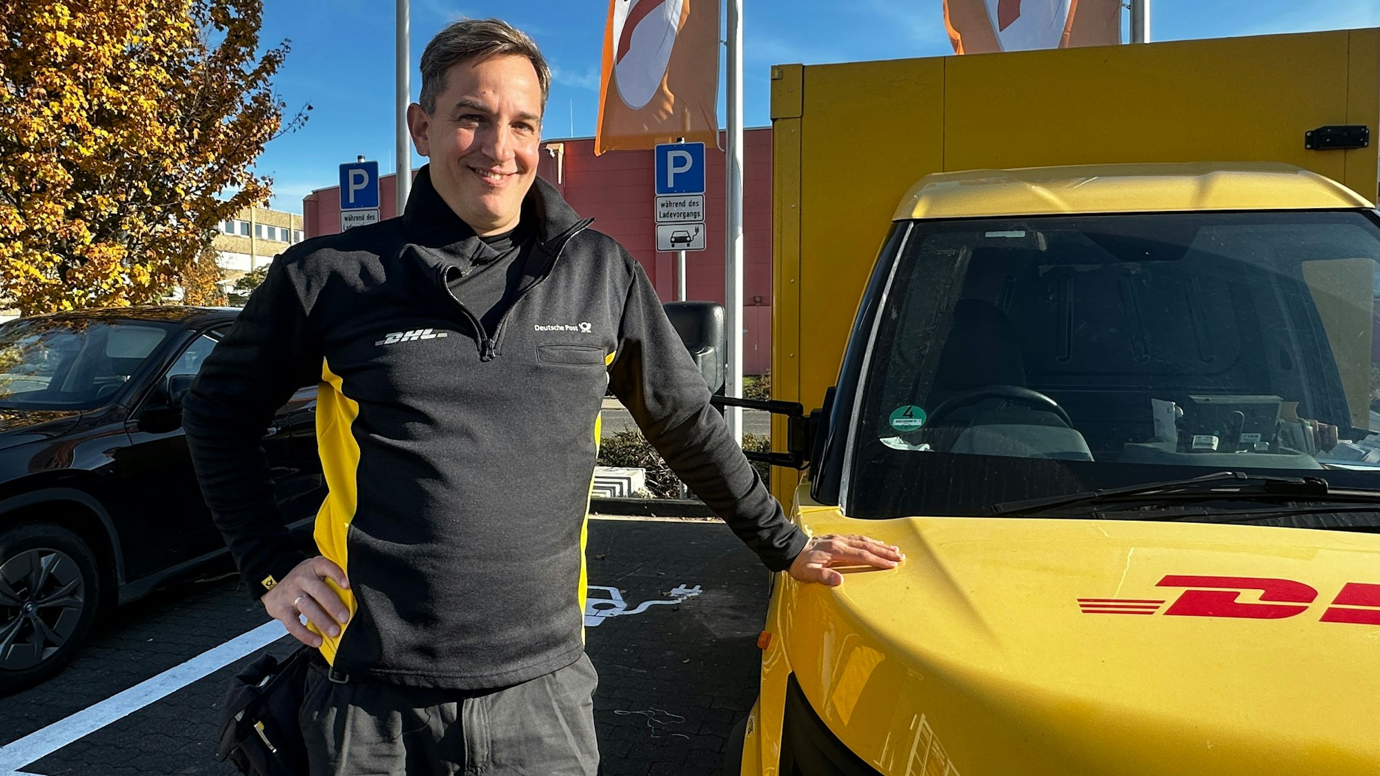 Ein Mann in Postuniform steht neben einem gelben DHL-Zustell-Transporter.
