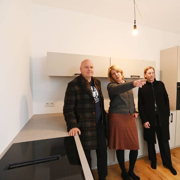 Drei Menschen stehen an eine Küchenzeile gelehnt in einem Haus.