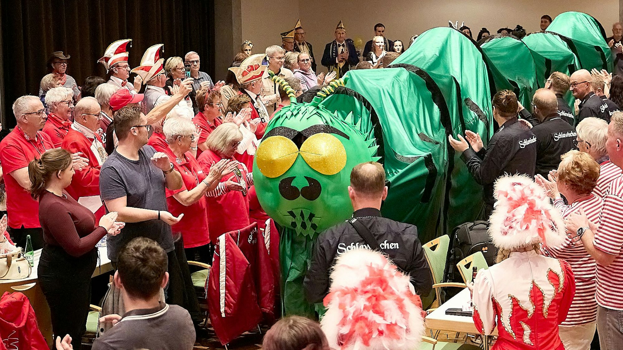Eine Tanzgruppe des Karnevalsvereins zieht unter einem grünen Tunnel, der aussieht wie eine Raupe, in den Kursaal in Gemünd ein.