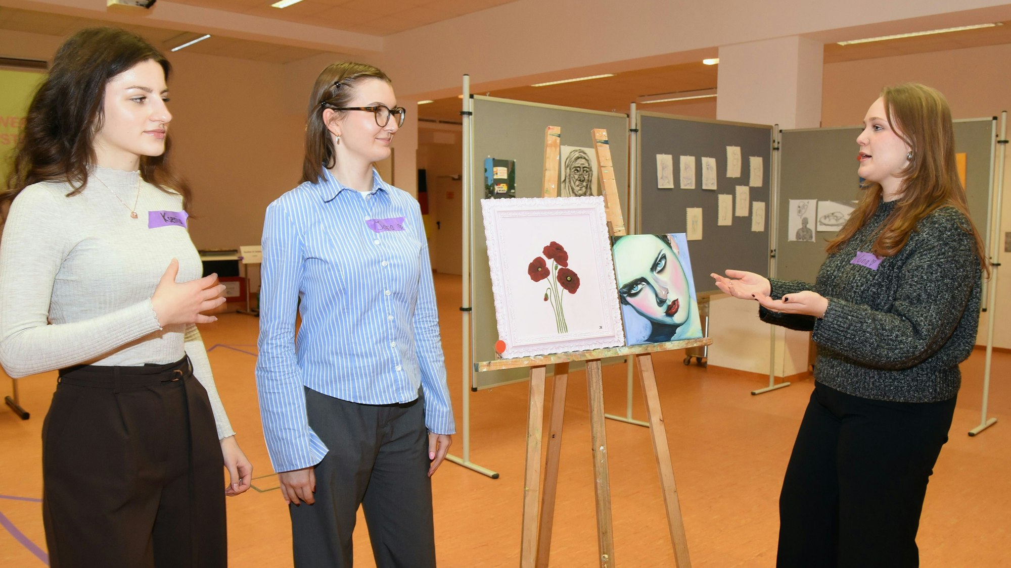 Drei junge Frauen stehen an einer Staffelei mit Bildern.