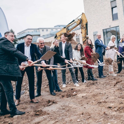 Zu sehen sind zahlreiche Frauen und Männer mit Spaten auf einer Baustelle.