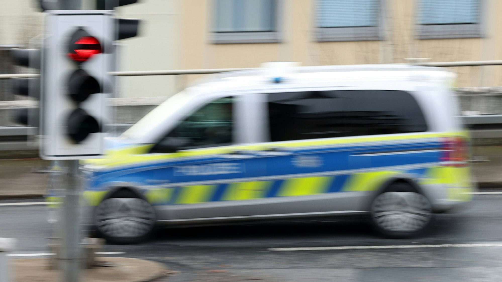 Ein Polizeiauto fährt mit Bewegungsunschärfe an einem Stoppschild und einer rot zeigenden Ampel vorbei.