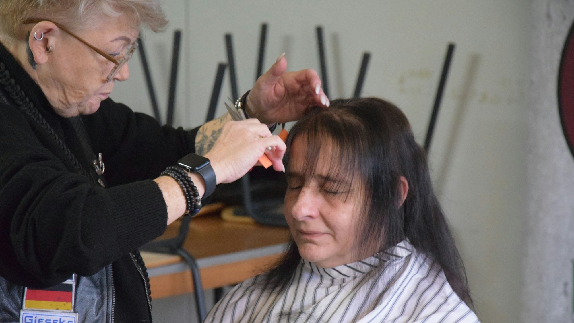 Eine ältere Friseurin schneidet einer Frau mit langem schwarzen Haar die Haare.