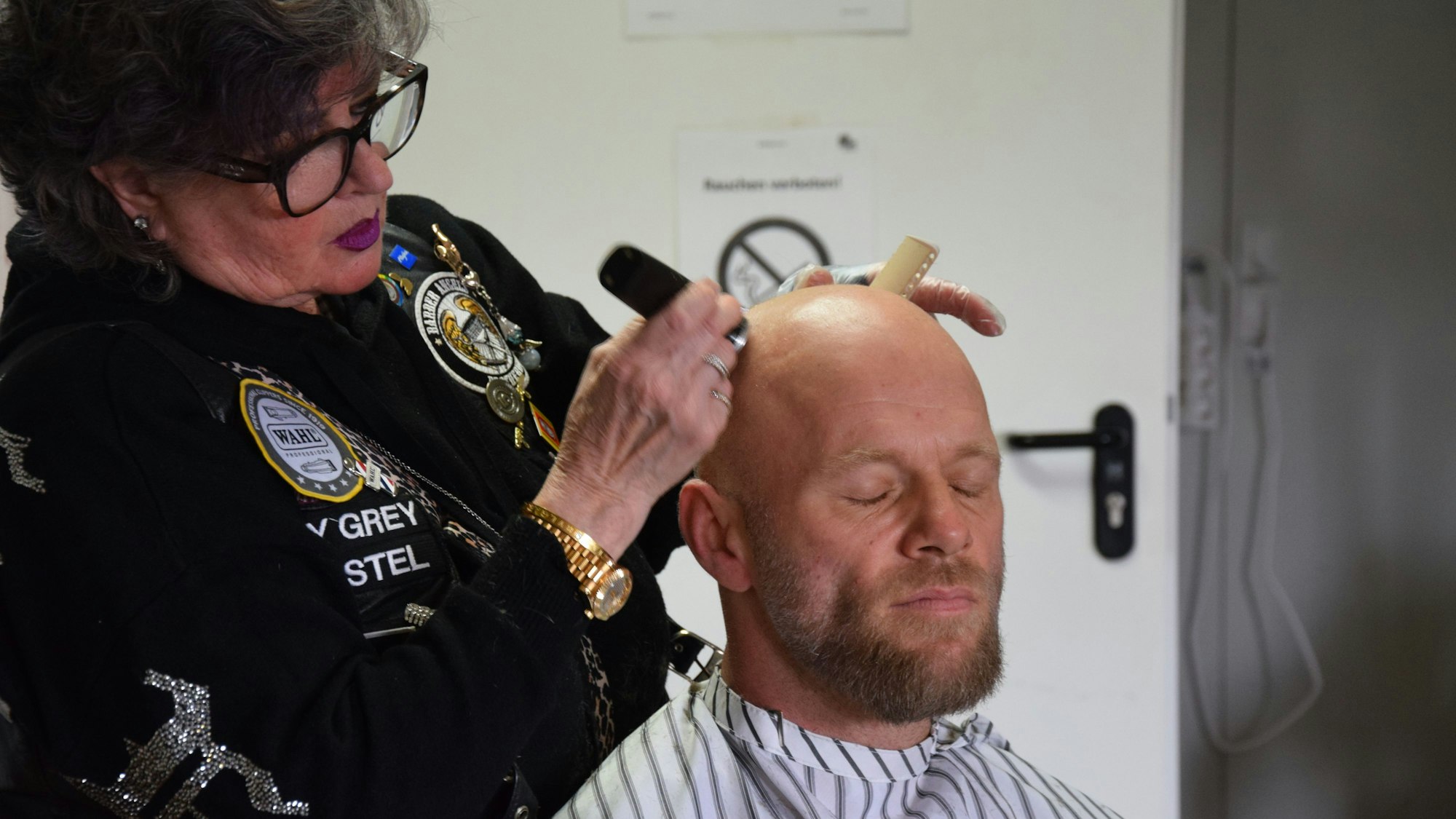 Eine Frau rasiert einem Mann den Kopf.