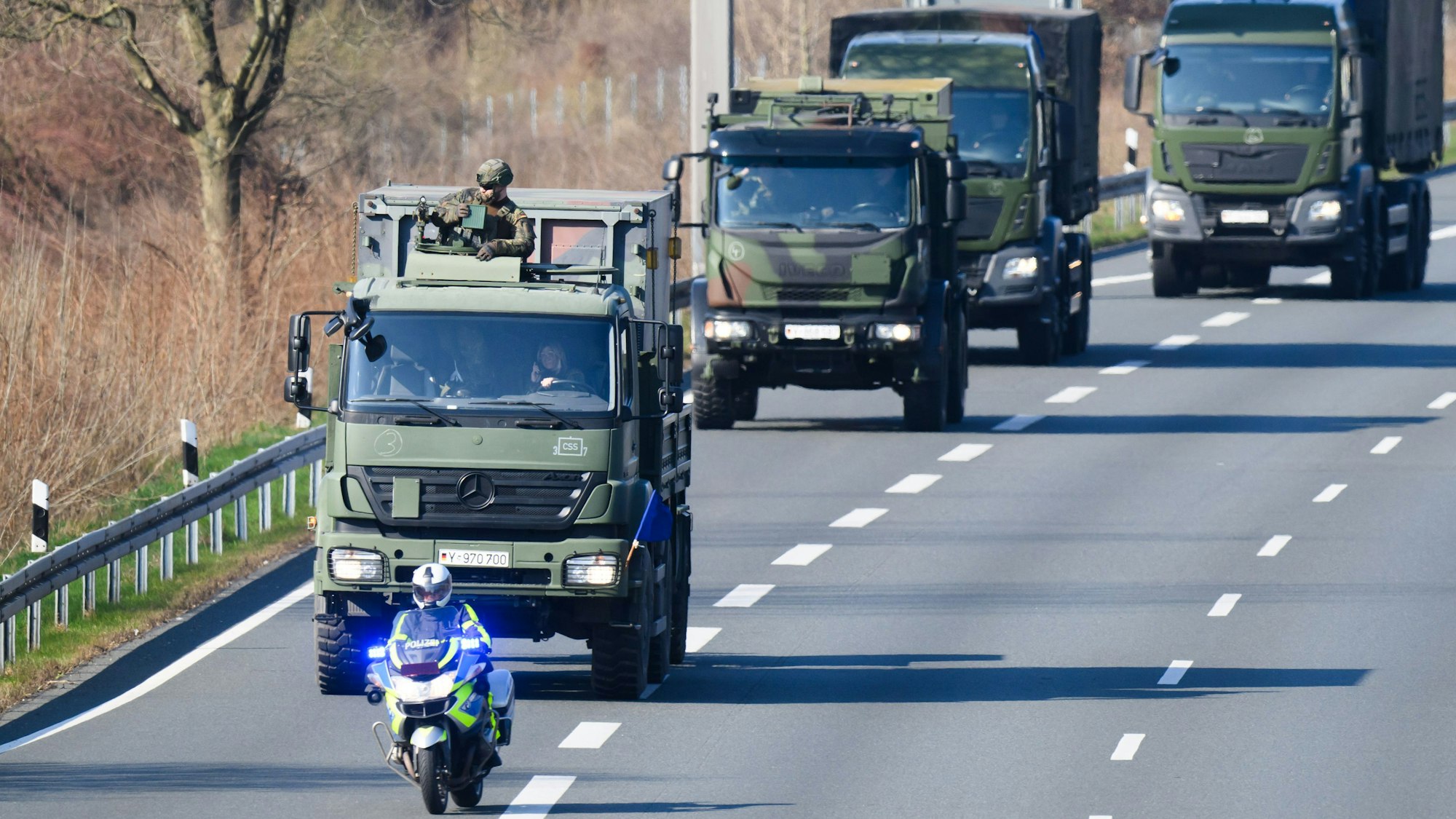 Das Symbolbild zeigt eine Kolonne mit Fahrzeugen der Bundeswehr und schwer bewaffneten Soldaten auf der Autobahn A2 im Norden von Hannover mit einem vorausfahrenden Polizeimotorrad.
