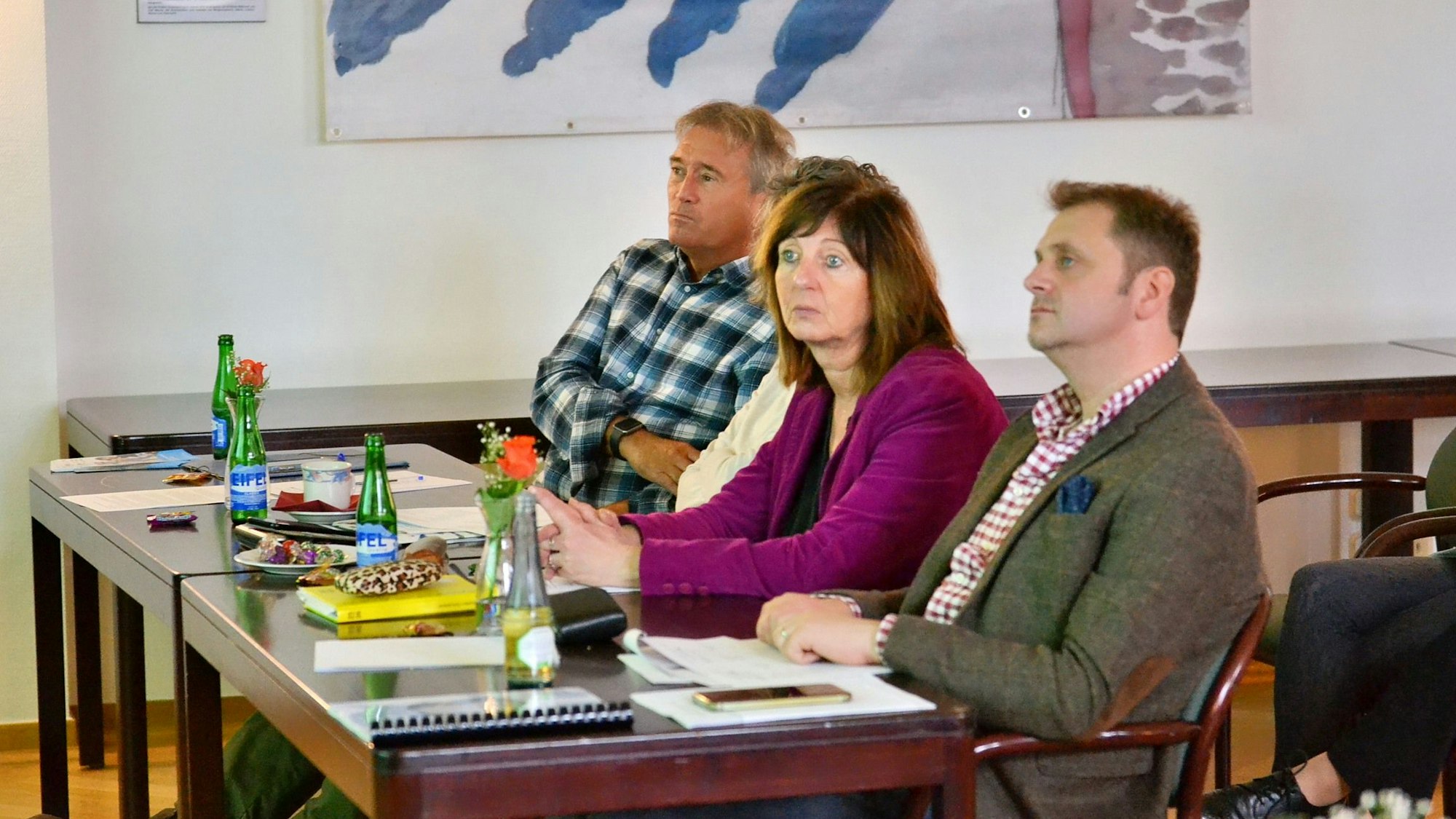 Zwei Männer und zwei Frauen (eine ist verdeckt) sitzen an einem Tisch.