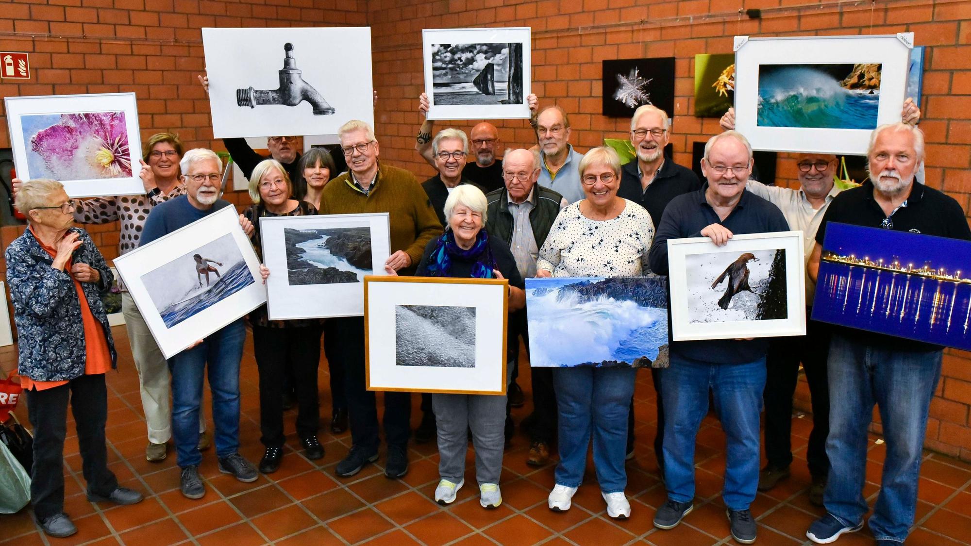 Zu sehen sind Frauen und Männer, die gerahmte Fotos halten.