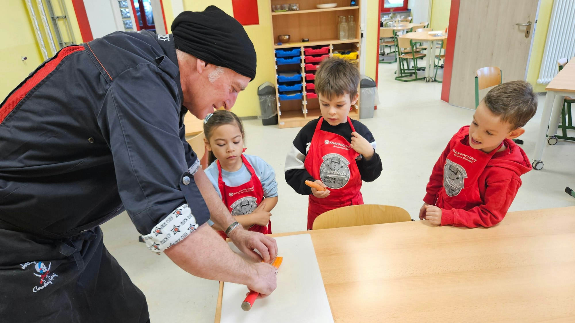 Wolfgang Marquard steht an einem Tisch und schneidet eine Möhre. Die Kinder schauen zu.