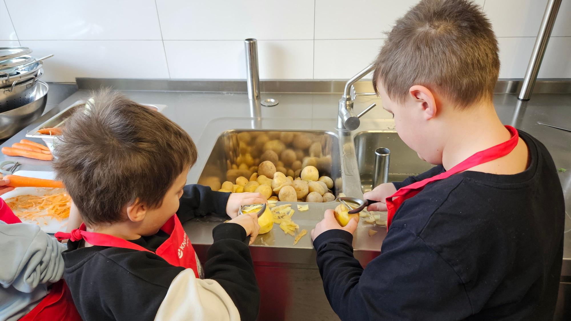 Zwei Jungen stehen an einer Spüle und schälen Kartoffeln.