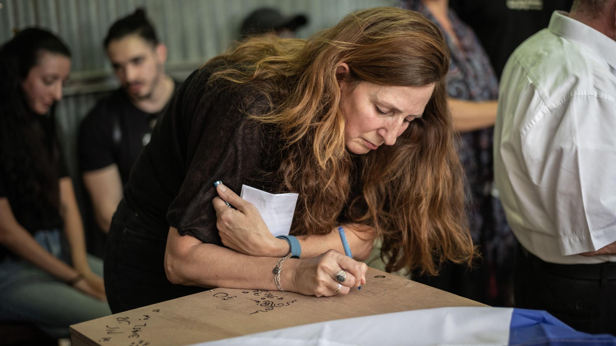 Ricarda Louk schreibt auf den mit einer Flagge bedeckten Sarg ihrer Tochter Shani Louk während ihrer Beerdigung.