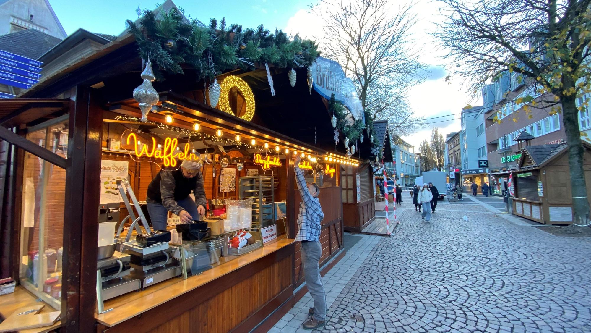 Zu sehen ist einer der Stände des Weihnachtsmarktes. Zwei Mitarbeiter sind mit dem Aufbauen beschäftigt.