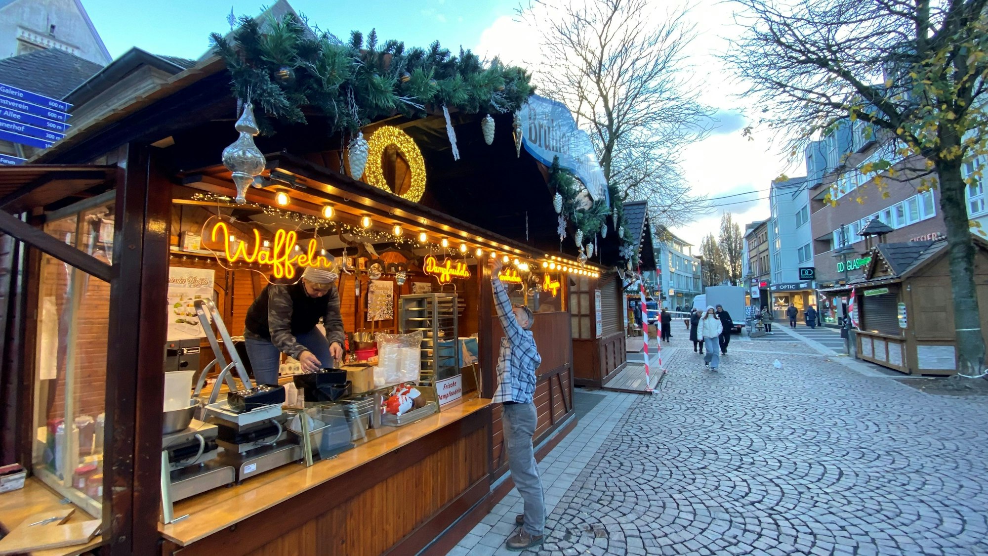 Zu sehen ist einer der Stände des Weihnachtsmarktes. Zwei Mitarbeiter sind mit dem Aufbauen beschäftigt.