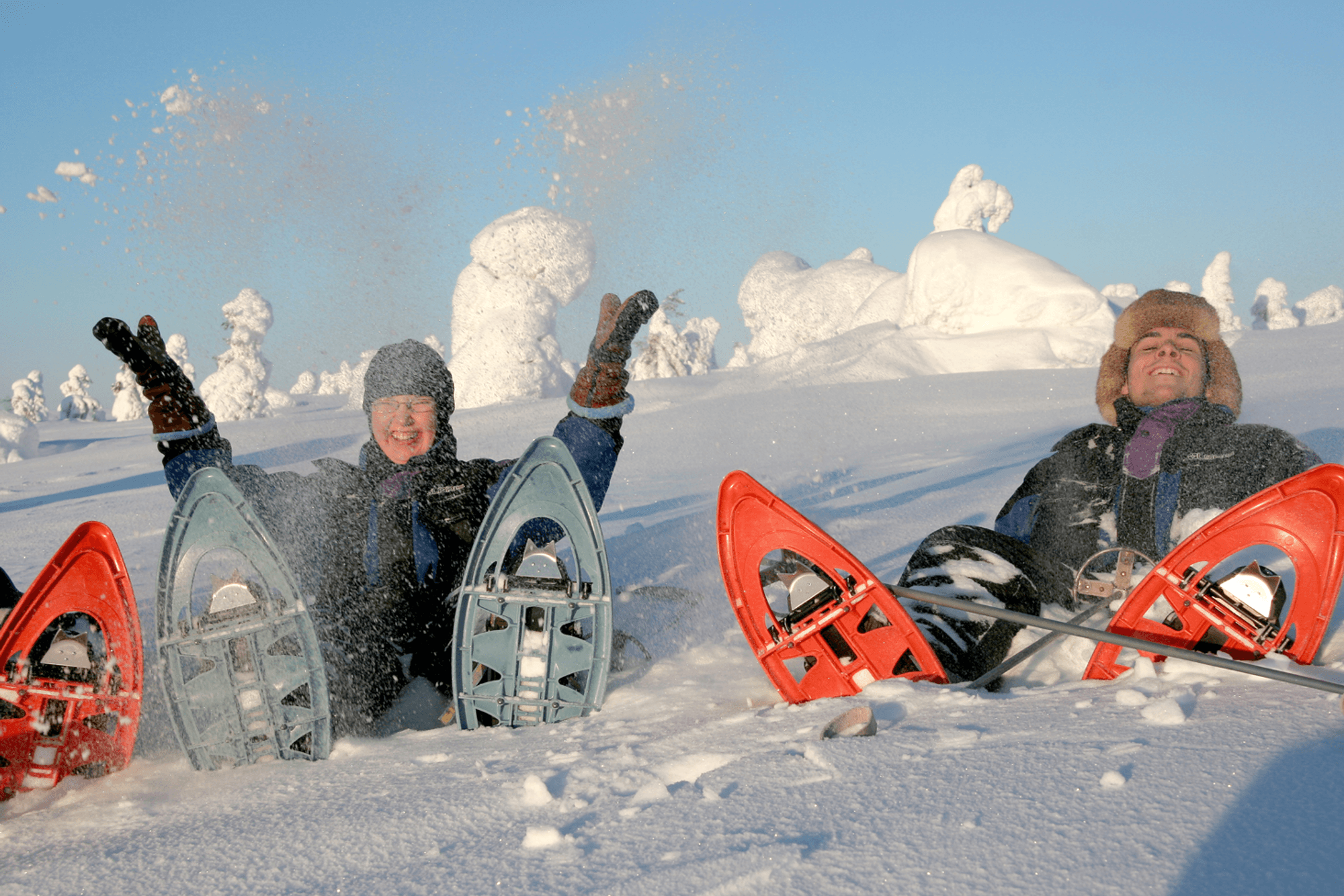 Das Bild zeigt zwei Personen, die während einer Schneeschuhwanderung im Schnee liegen und Spaß haben.