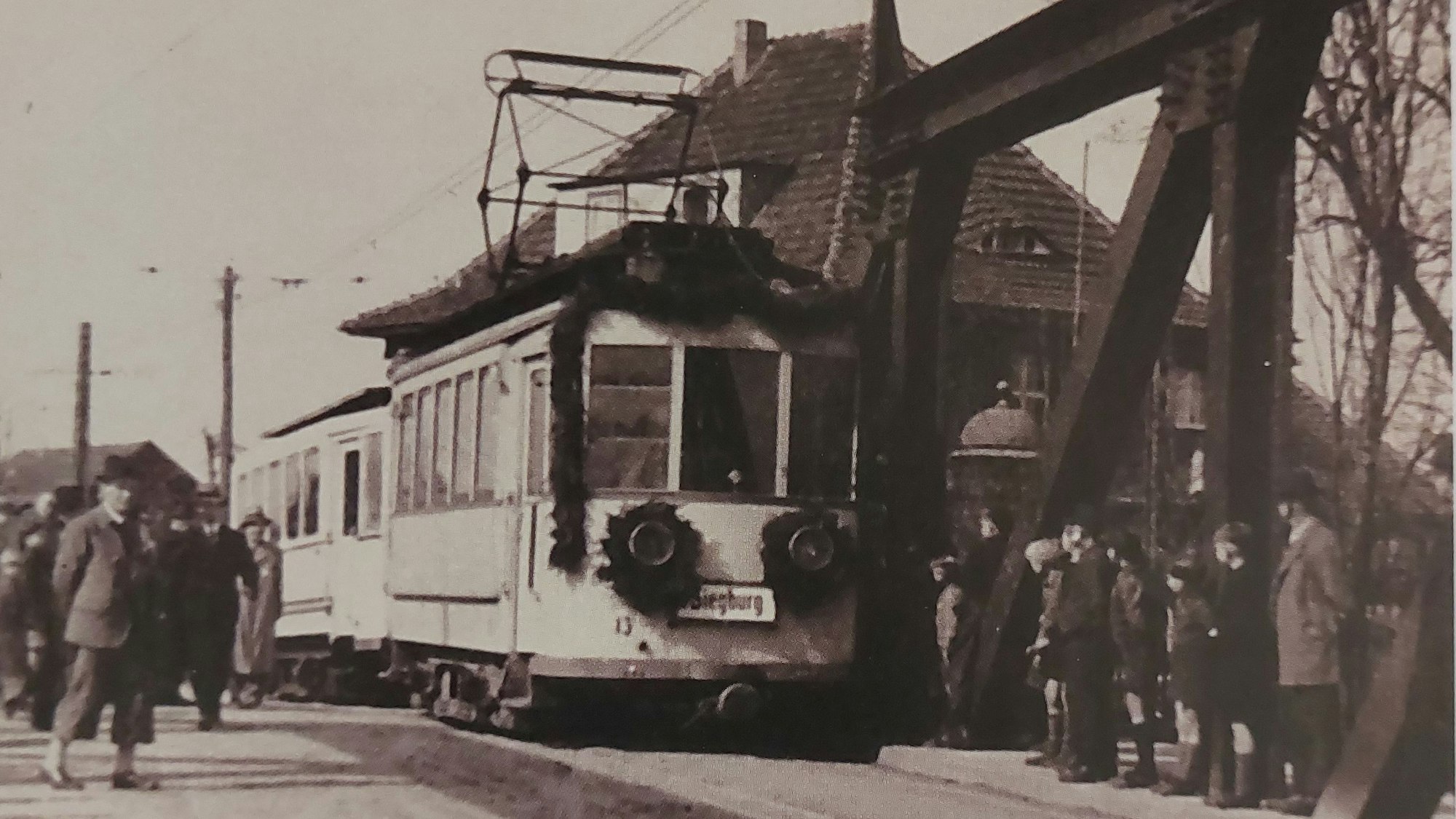 Historische Schwarz-Weiß-Aufnahme einer mit Girlande geschmückten Straßenbahn.