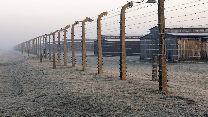 Häftlingsbaracken des ehemaligen Konzentrationslagers Auschwitz-Birkenau hinter einem hohen Stacheldrahtzaun, Landschaft
