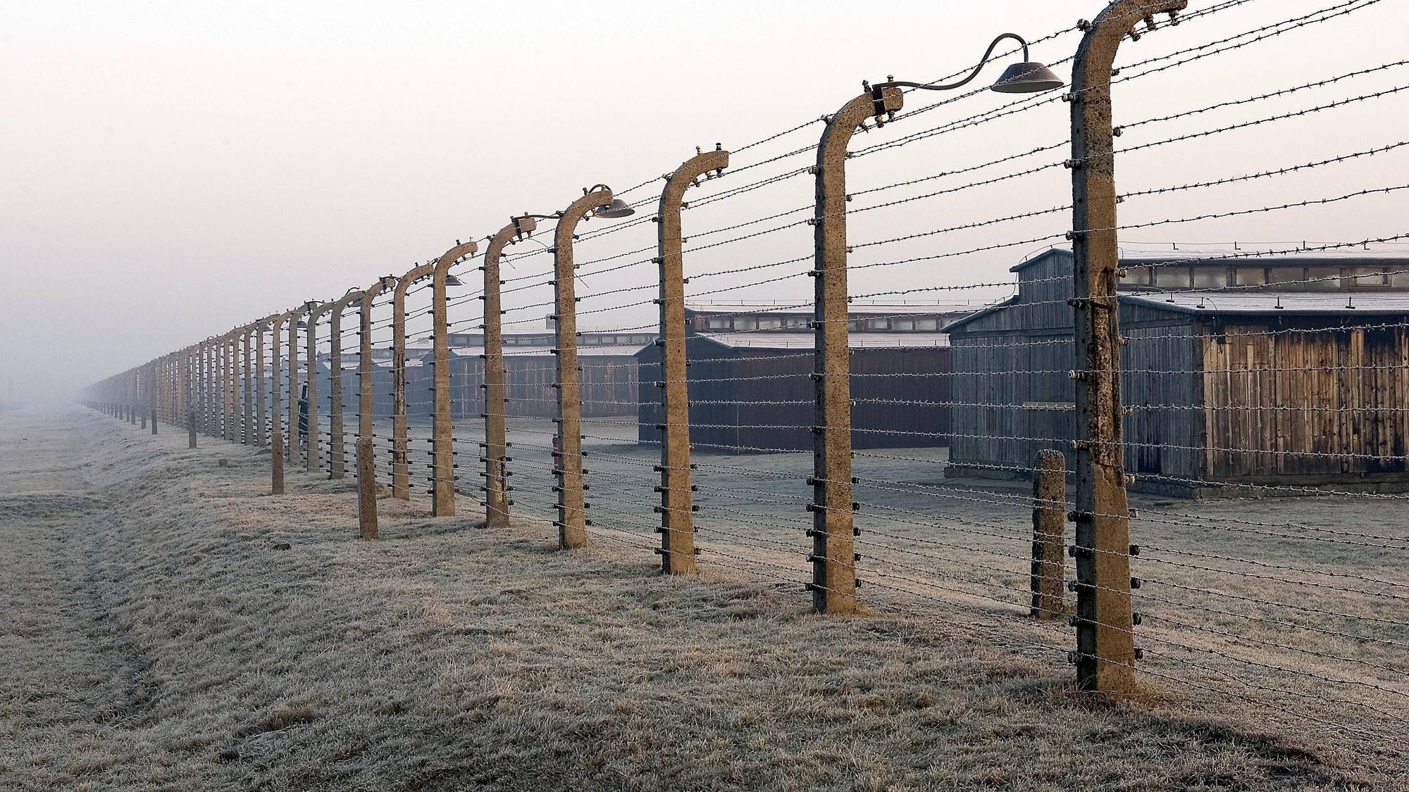 Häftlingsbaracken des ehemaligen Konzentrationslagers Auschwitz-Birkenau hinter einem hohen Stacheldrahtzaun, Landschaft