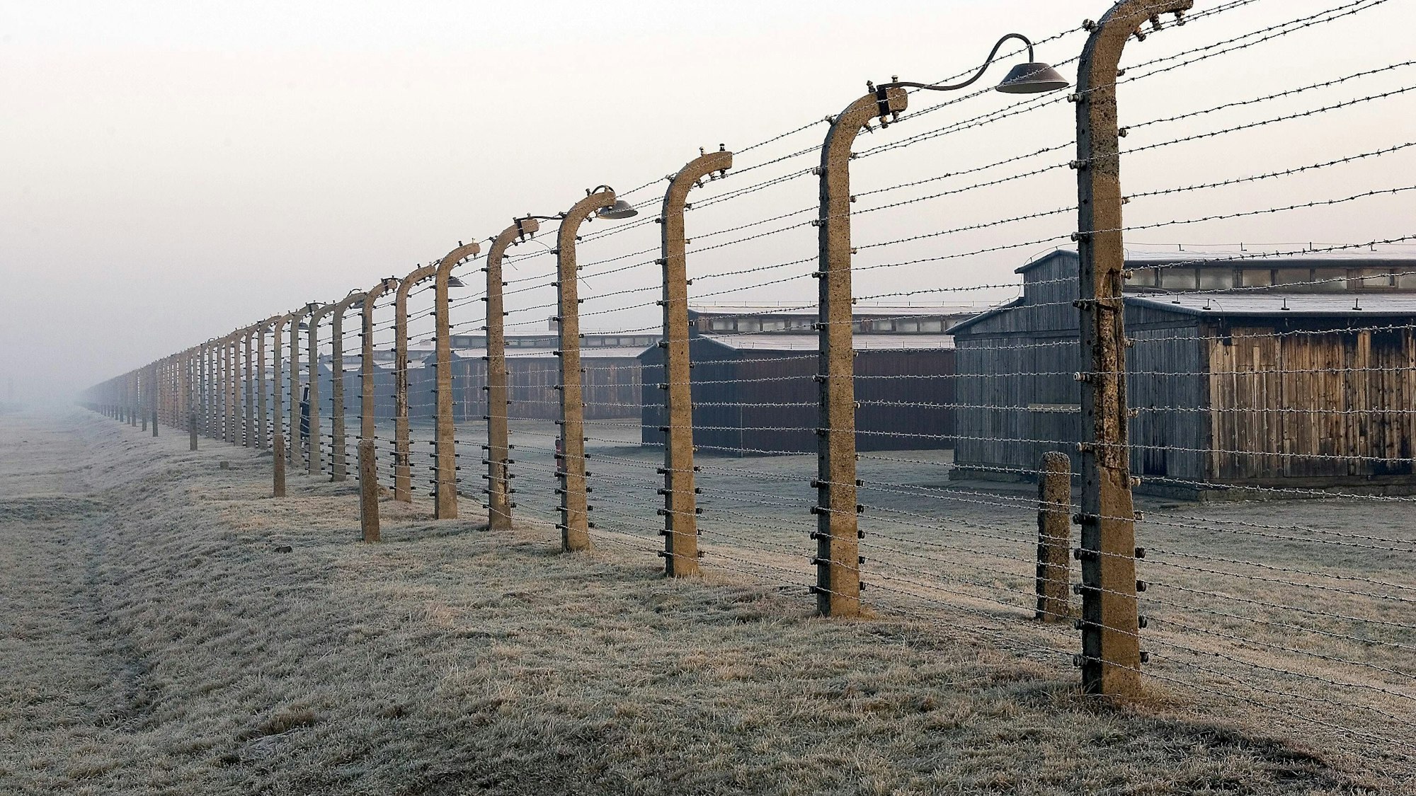 Häftlingsbaracken des ehemaligen Konzentrationslagers Auschwitz-Birkenau hinter einem hohen Stacheldrahtzaun, Landschaft
