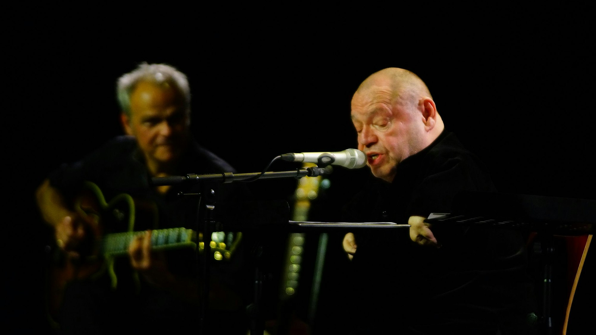 Auf dem Bild sind zwei Musiker auf einer Bühne zu sehen.