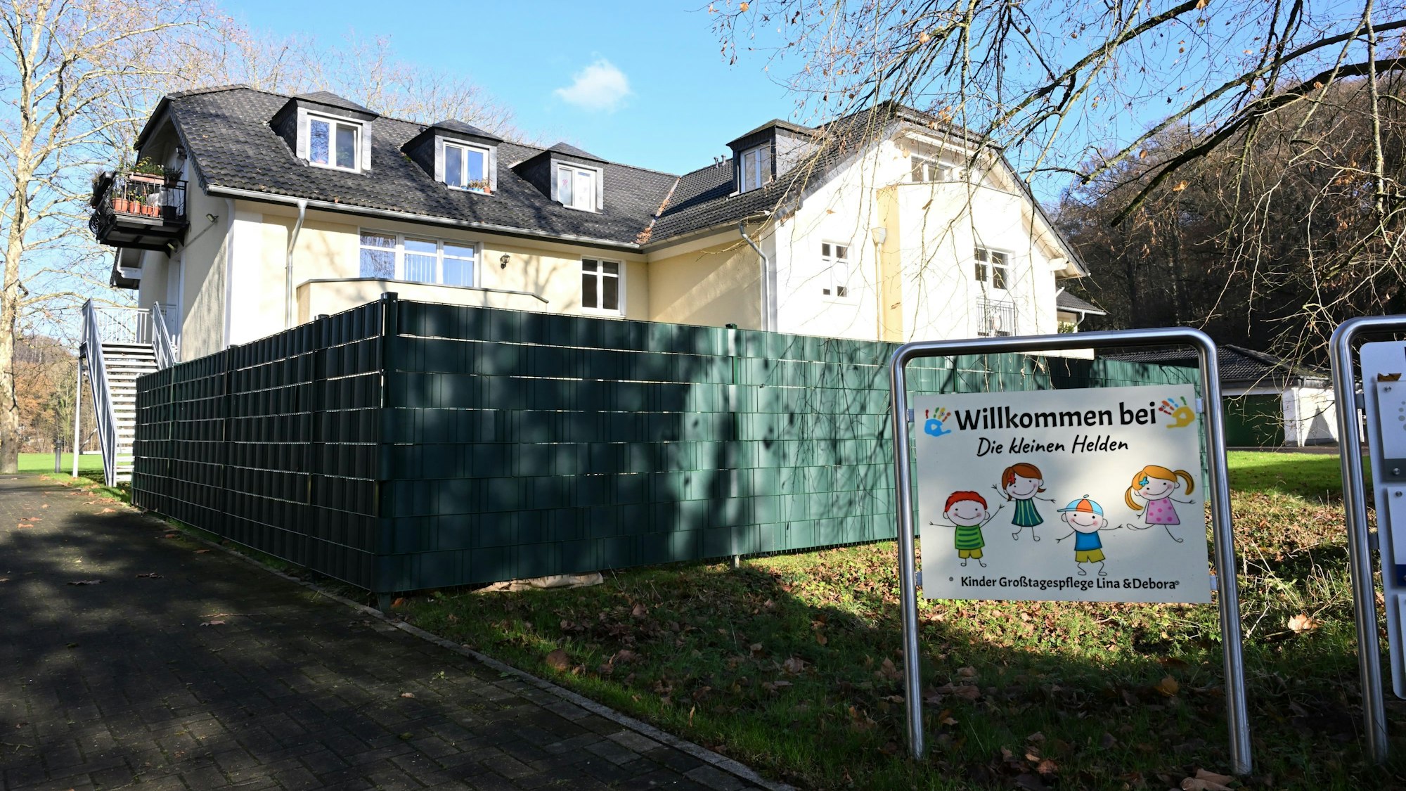 Ein Haus, davor ein Sichtschutz und ein Schild mit der Aufschrift: Willkommen bei „Die kleinen Helden“