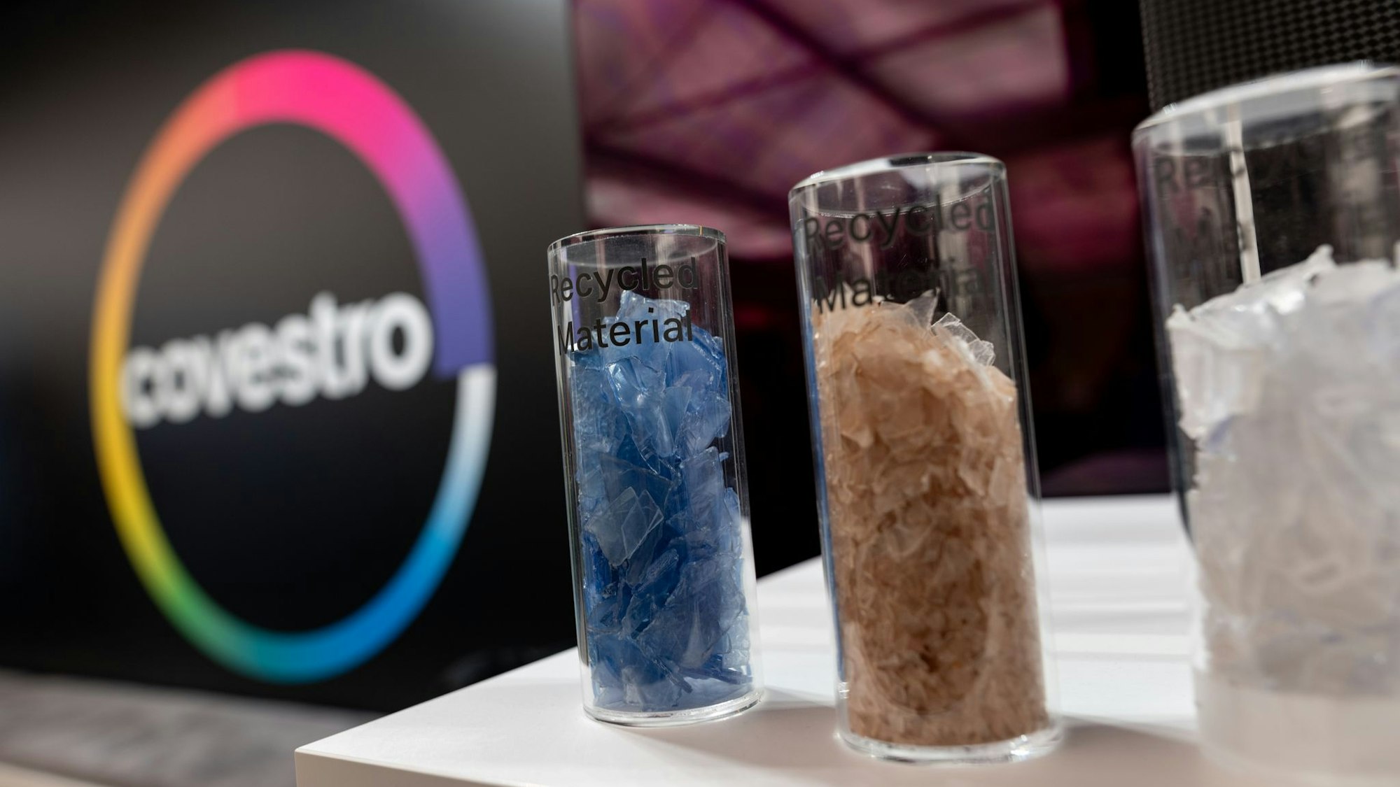 Eine deutsche Firma wird arabisch: Das Logo des Spezialchemie-Konzerns in einem Firmen-Showroom, davor Gläser mit Covestro-Materialien.