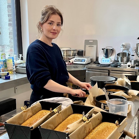 Eine Frau steht in einer Backstube. Auf einem Arbeitstisch stehen verschiedene gefüllte Teigformen.