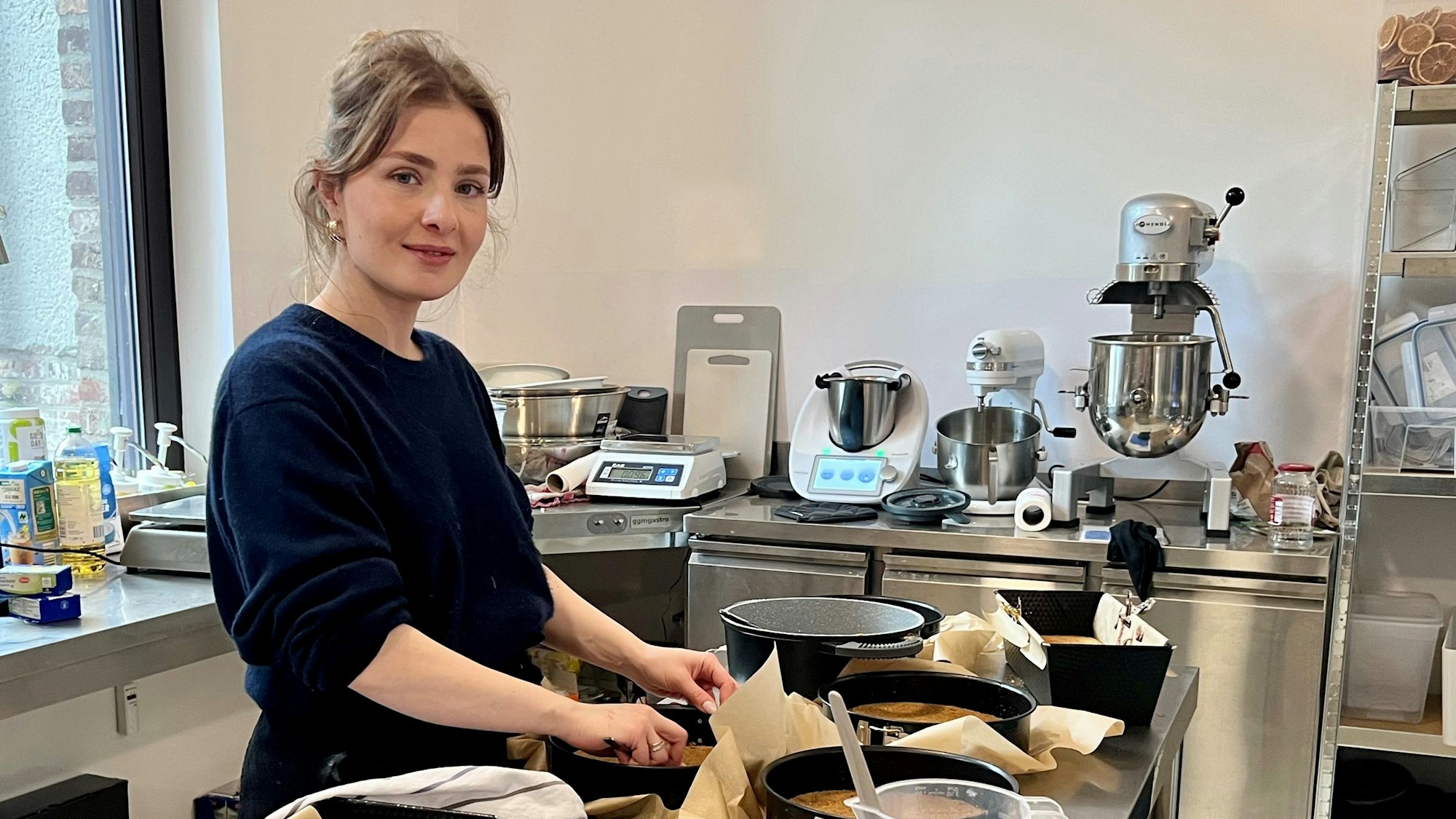 Eine Frau steht in einer Backstube. Auf einem Arbeitstisch stehen verschiedene gefüllte Teigformen.