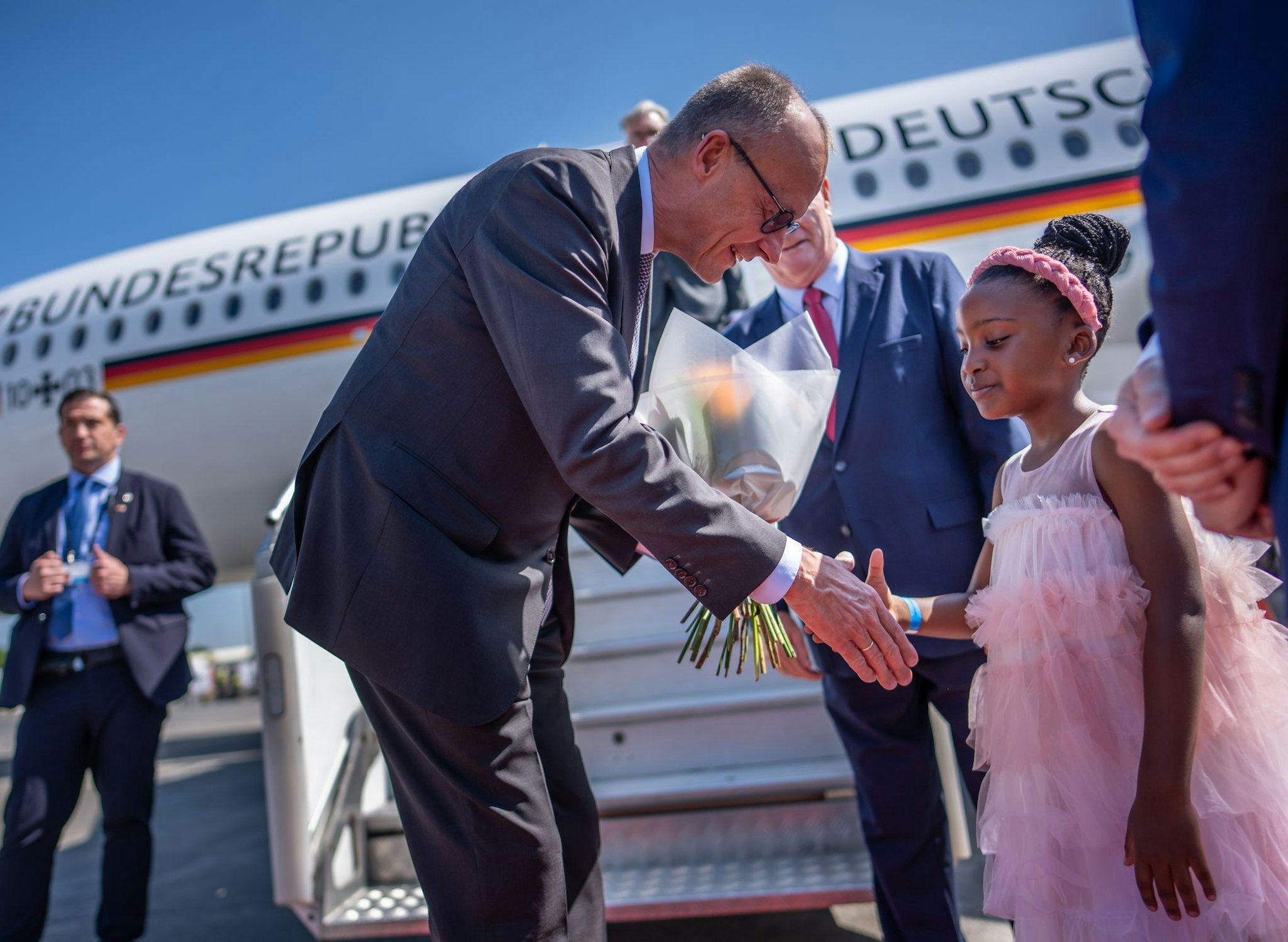 Kanzler Friedrich Merz wird auf dem Flughafen von Johannesburg von einem Mädchen begrüßt.