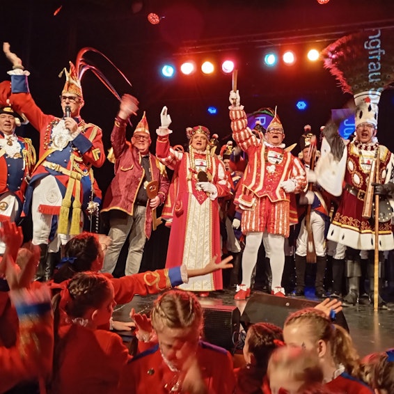 Ein Dreigestirn und weitere Karnevalisten stehen auf einer Bühne.