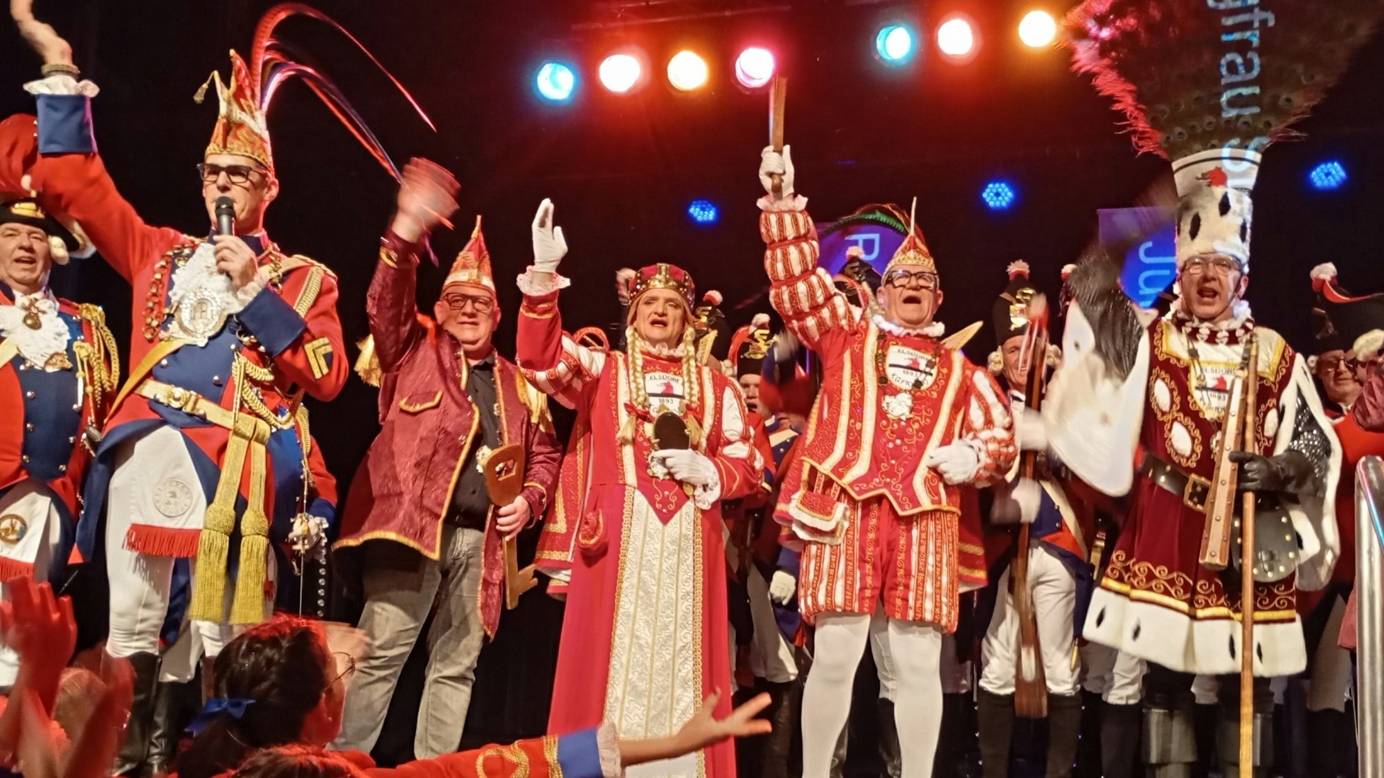 Ein Dreigestirn und weitere Karnevalisten stehen auf einer Bühne.