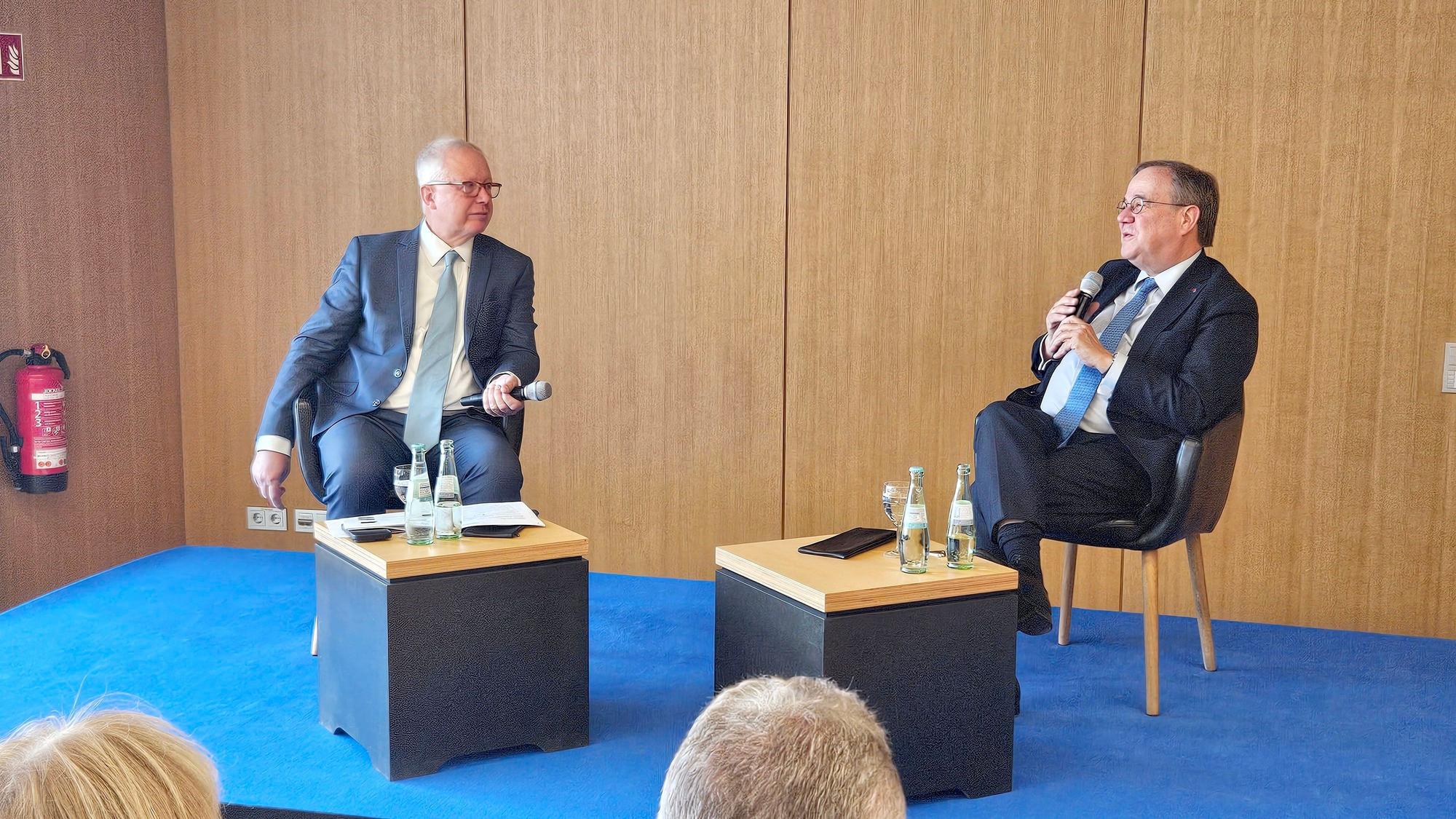 Tom Buhrow und Armin Laschet sitzen an zwei kleinen Tischen und haben jeder ein Mikro in der Hand.