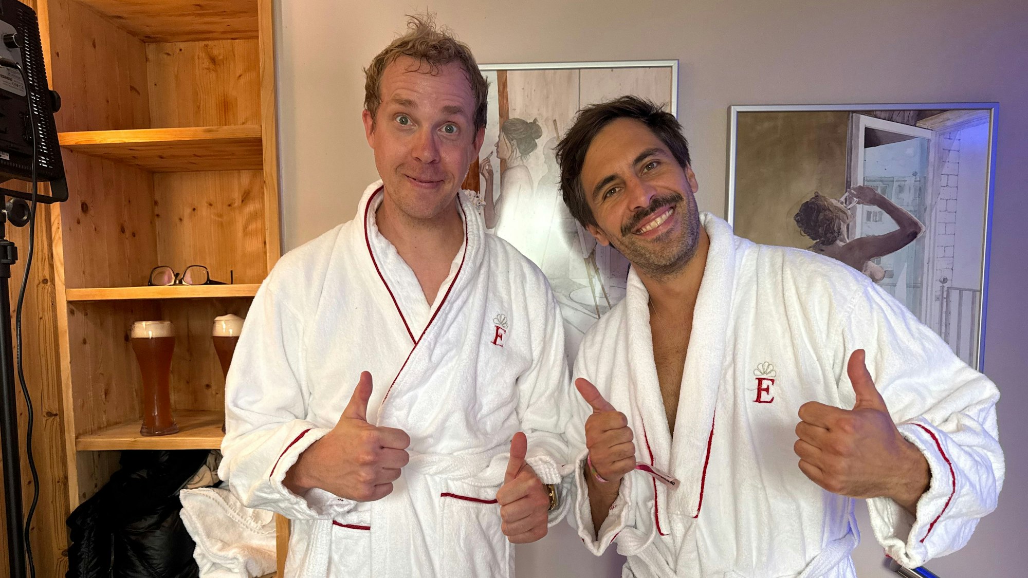 Daniel Schlipf und Max Giesinger stehen nebeneinander im Bademantel und halten die Daumen hoch.
