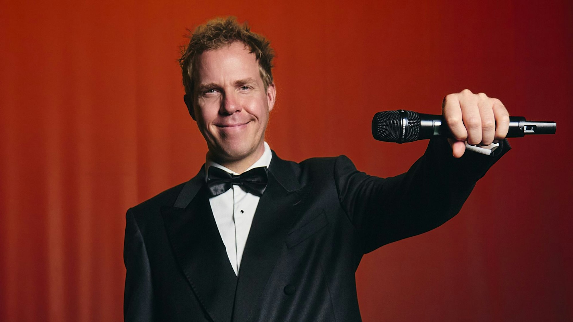 Daniel Schlipf im Smoking mit einem Mikrofon in der Hand.