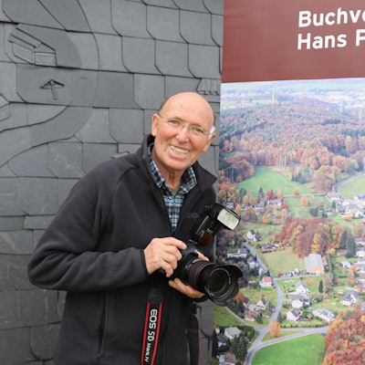 Hans-Peter Barrig hat ein gut 500 Seiten starkes Buch über sein Heimatdorf Käsberg geschrieben. Der Autor vor dem Cover seines Buchs auf einem Roll-up.