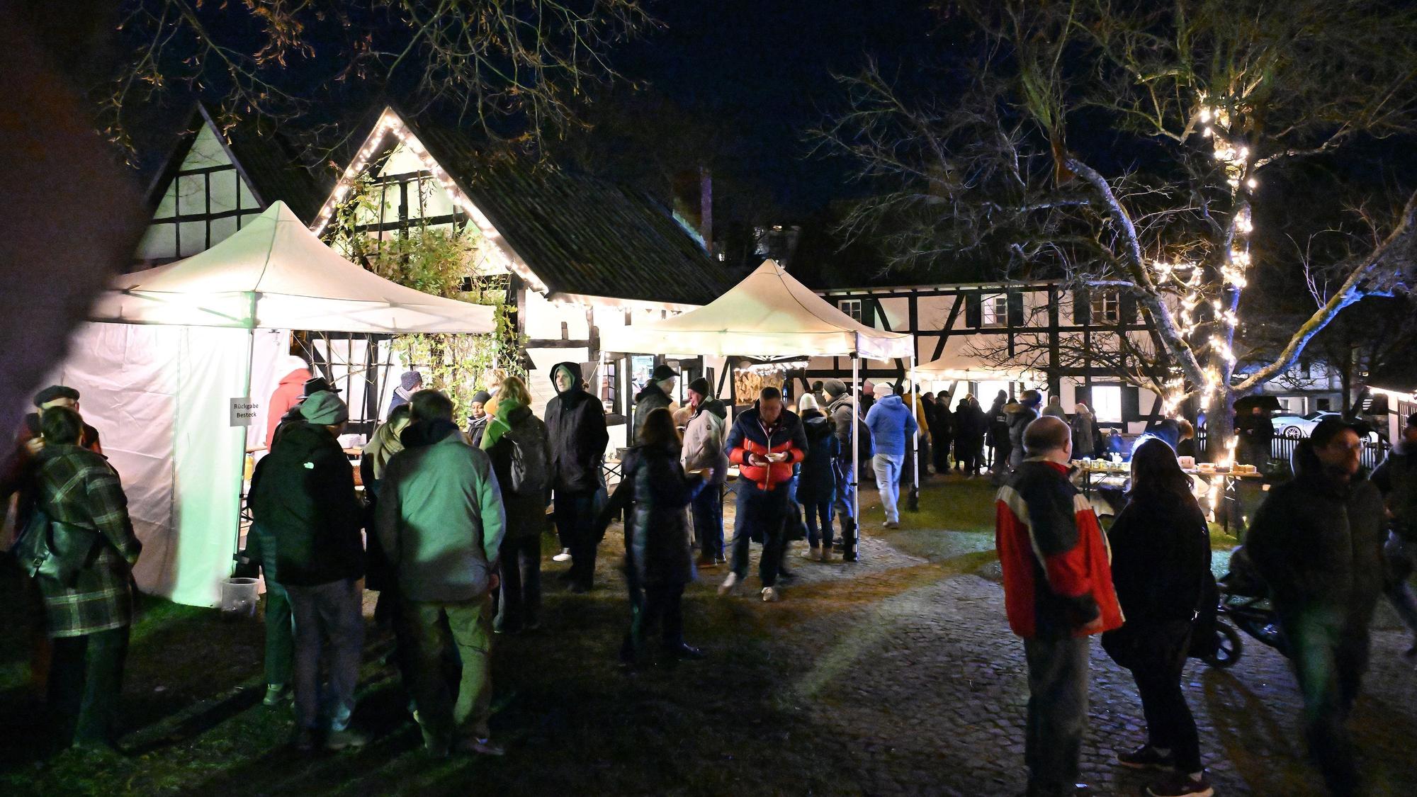 Menschen stehen und gehen zwischen Ständen neben Fachwerkhäusern im Bergischen Museum in Bensberg