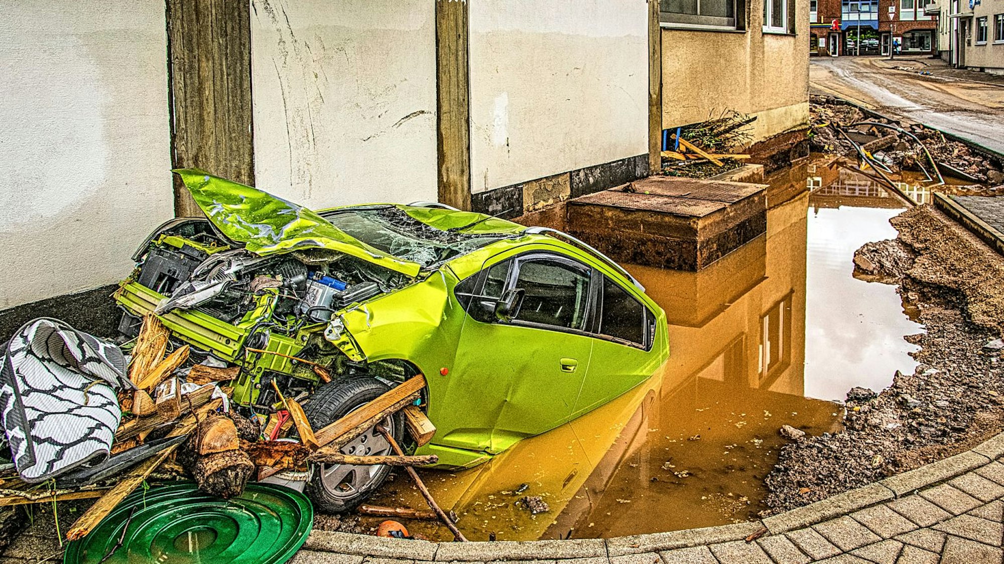 Ein grellgrünes Auto steckt mit dem Heck in einem mit Wasser gefüllten Loch, das sich vor einem Haus gebildet hatte.
