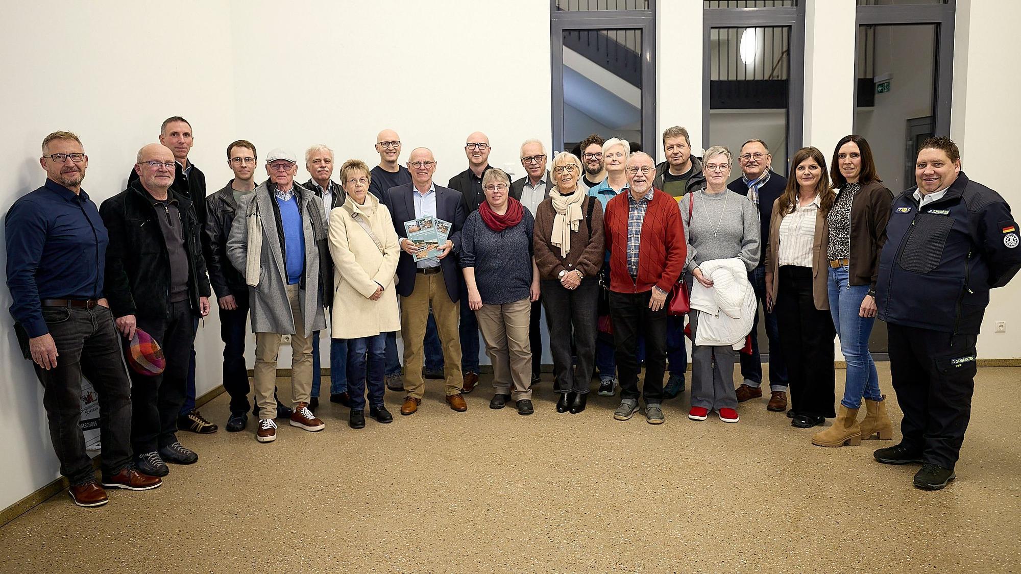 Eine Gruppe von Menschen steht nebeneinander, einer hält den BIldband in die Kamera.