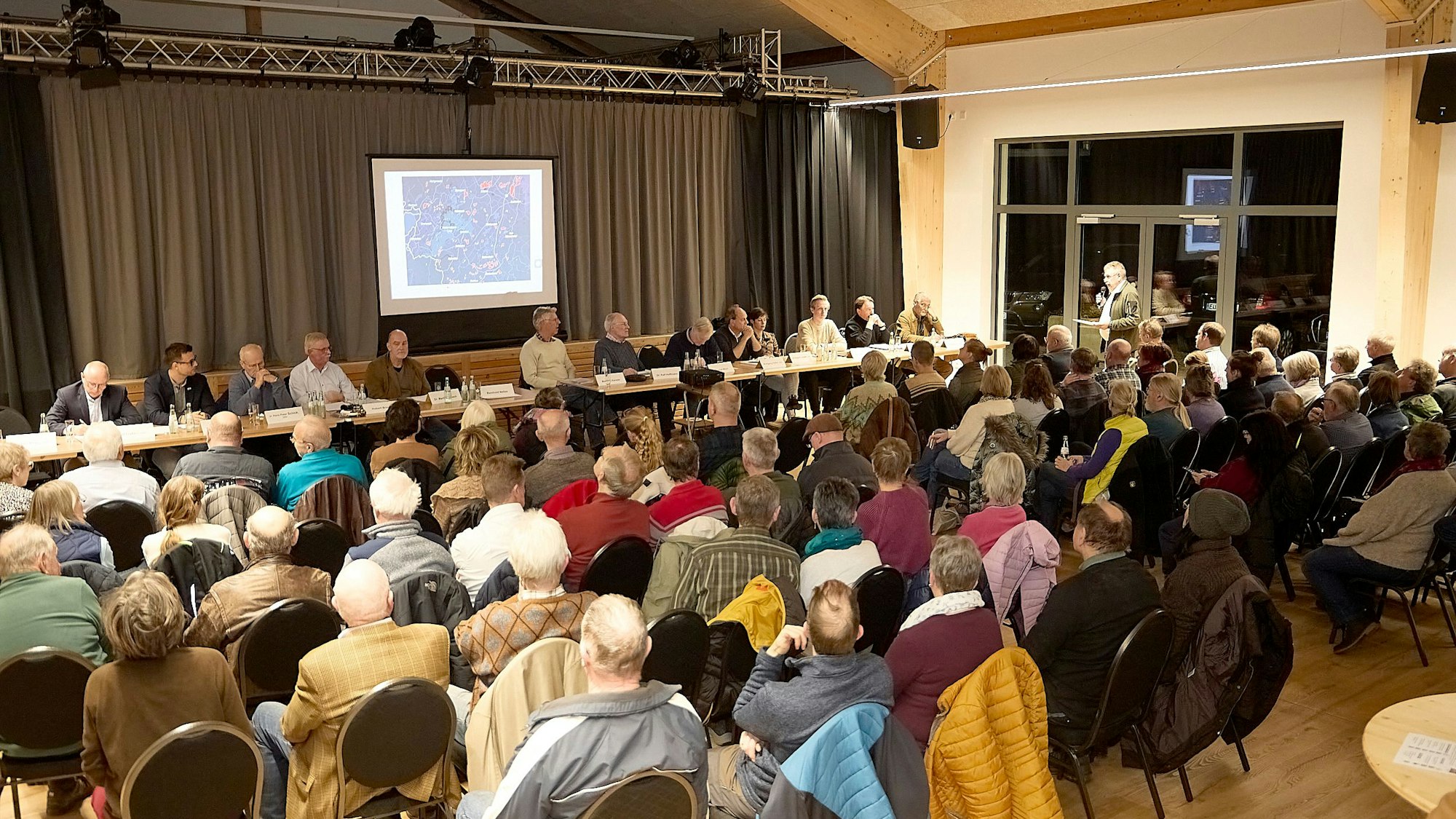 Das Bild zeigt die besetzten Stuhlreihen und das Podium.
