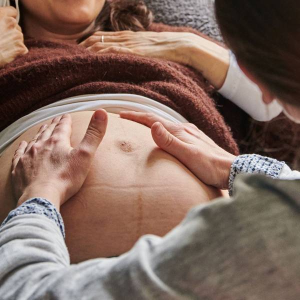Eine Hebamme tastet in ihrer Praxis den Bauch einer schwangeren Frau ab.