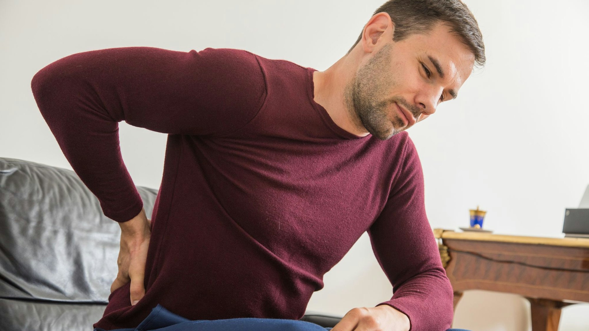 Ein Mann sitzt auf dem Sofa und hält sich den Rücken.