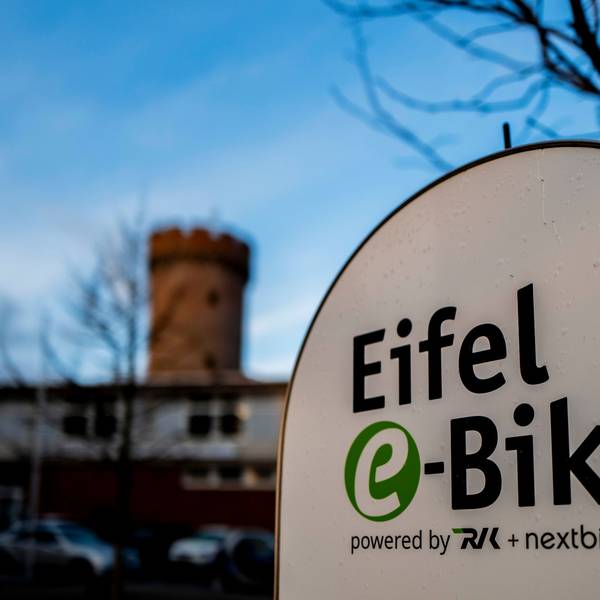 Das Bild zeigt im Vordergrund das Logo des Eifel-E-Bikes, im Hintergrund leicht unscharf die Zülpicher Landesburg.